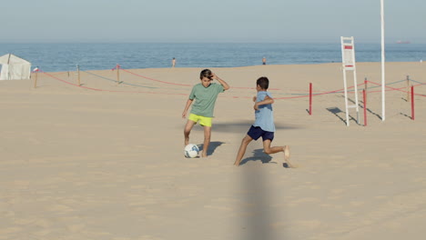 Long-shot-of-happy-teenagers-playing-football-on-sandy-beach